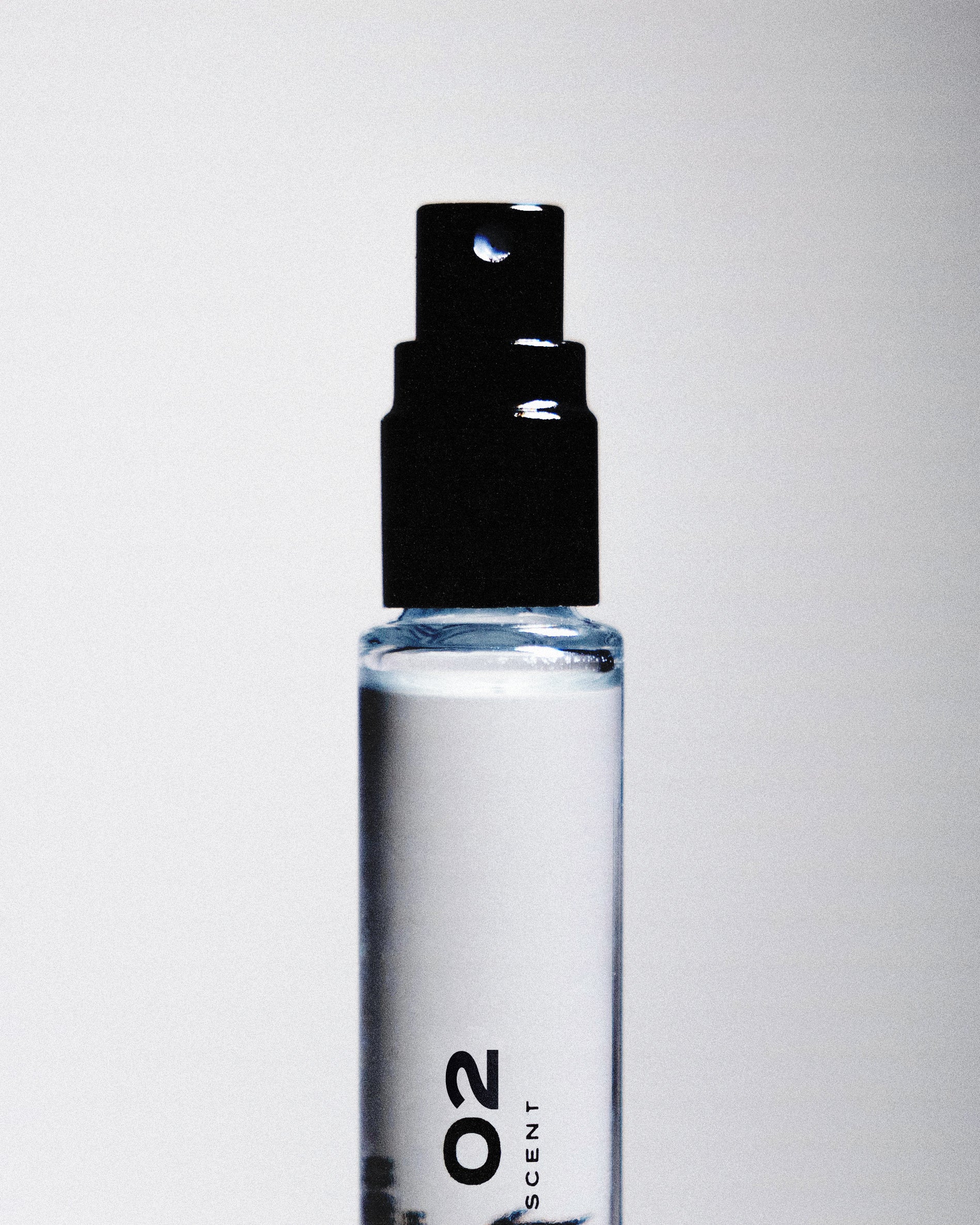Close up of a black perfume sprayer with "02" written on the glass bottle against a white backdrop. 