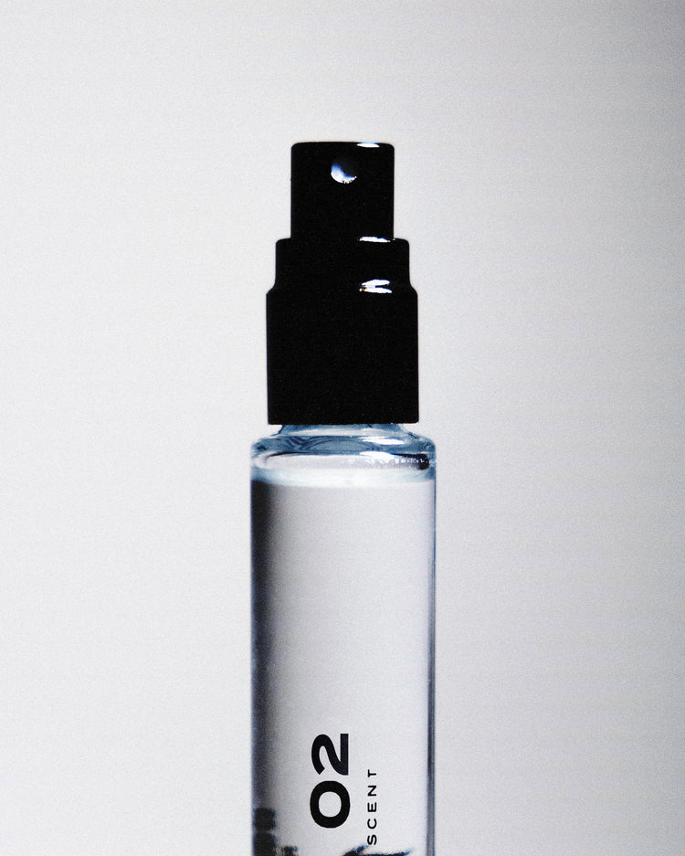 Close up of a black perfume sprayer with "02" written on the glass bottle against a white backdrop. 