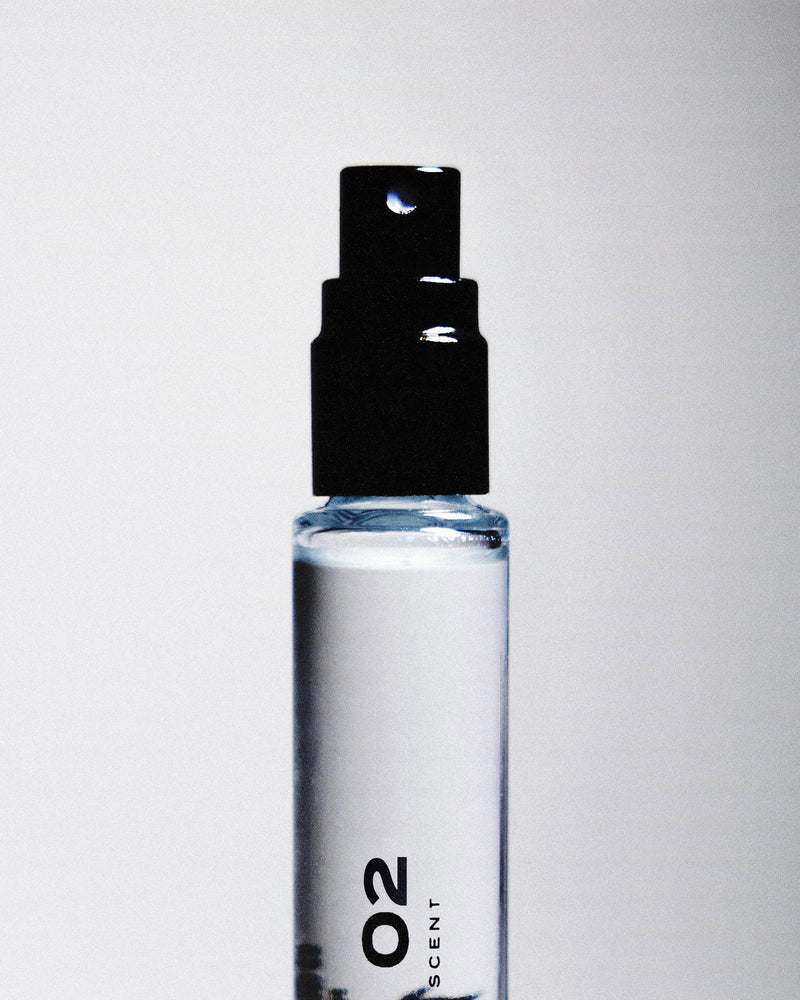 Close up of a black perfume sprayer with "02" written on the glass bottle against a white backdrop. 