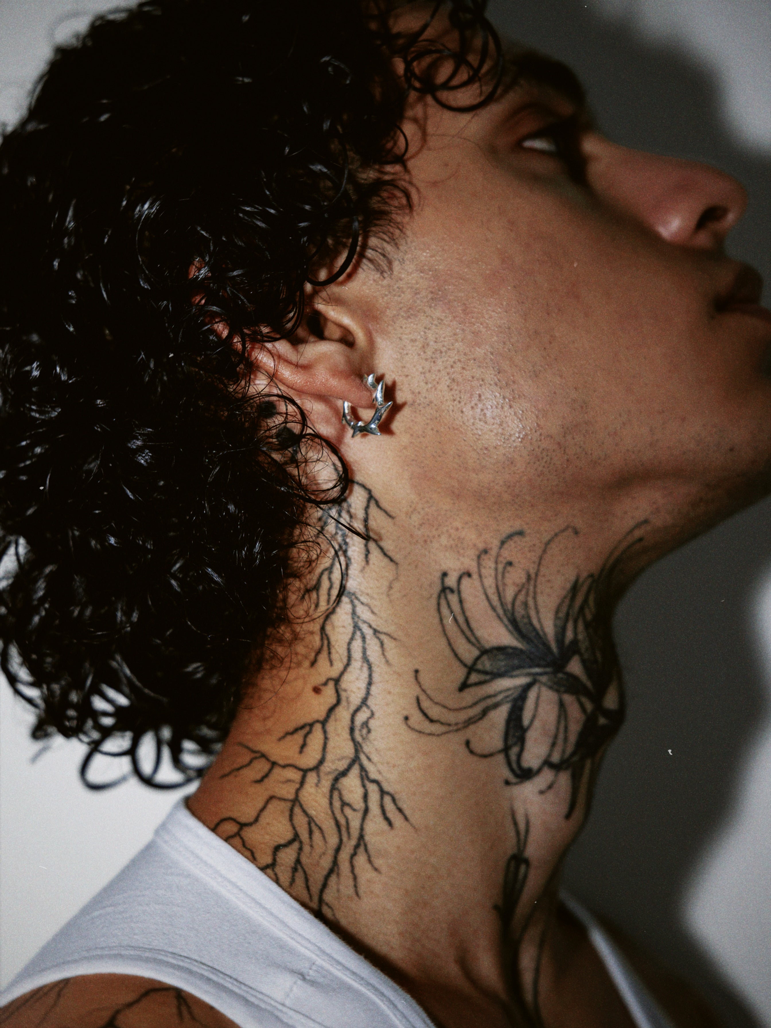 Portrait of a male model with neck tattoos wearing a silver spiked hoop earring against a white backdrop. 